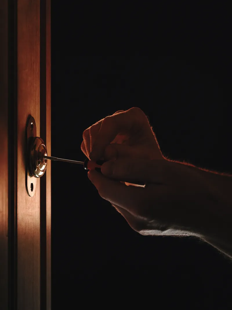 Hands fitting a deadbolt cylinder into a timber door edge, lit by a single orange light